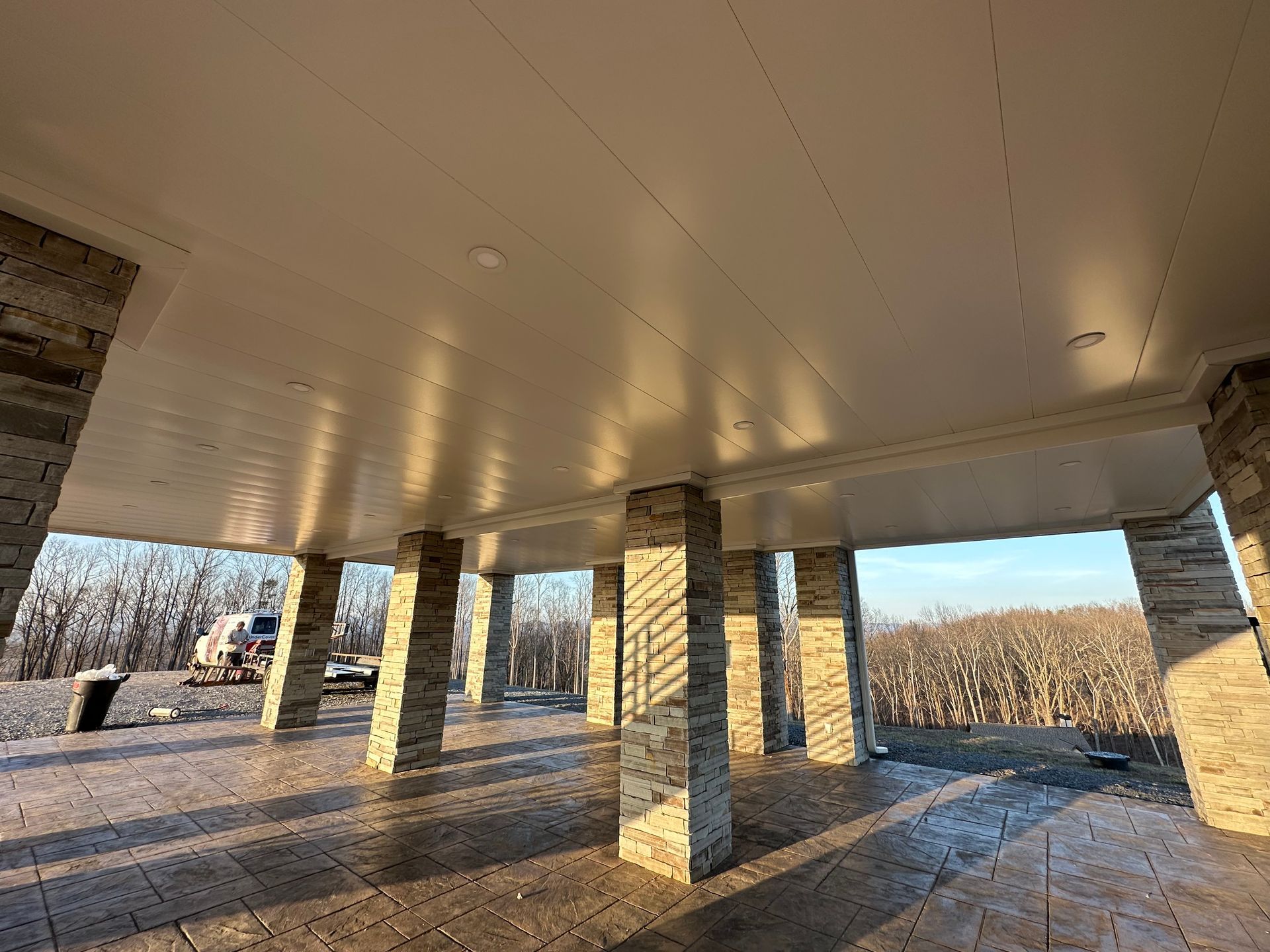 Underside of a large covered patio with stone columns, a light-colored ceiling, and an outdoor view.