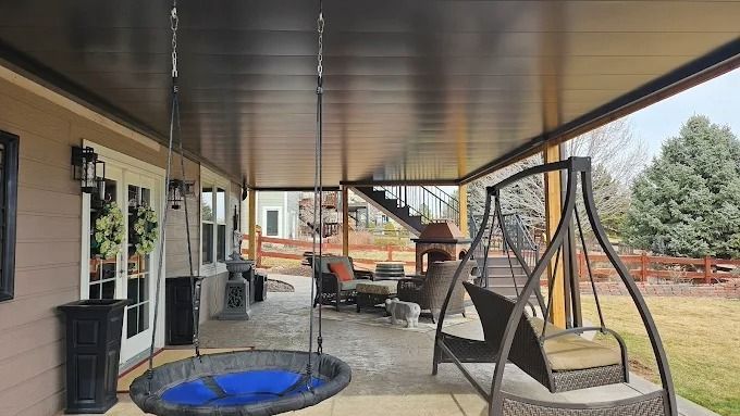 Two-story house with a covered patio, stone facade, and upper deck. Gray and beige exterior with outdoor seating.