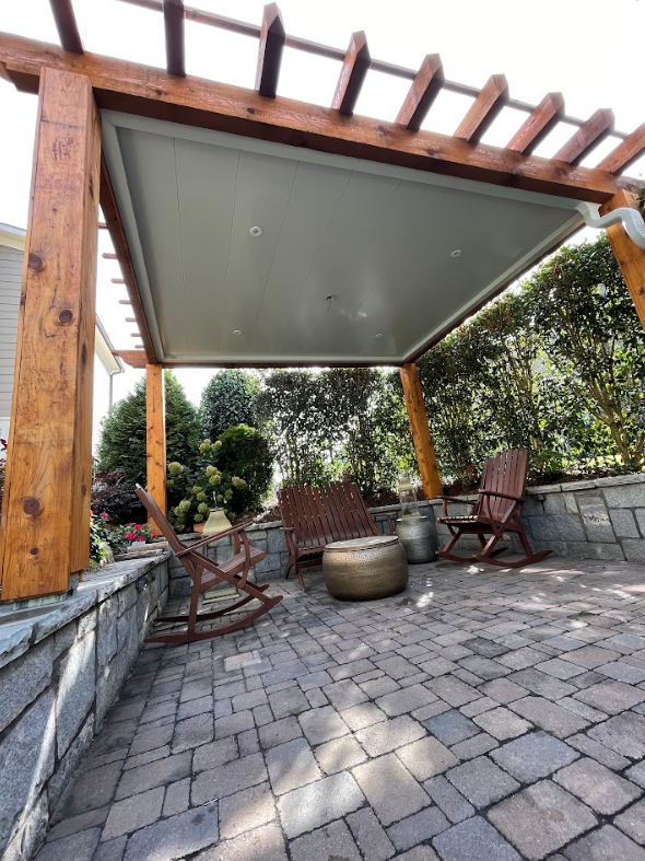 Patio with wooden pergola, gray ceiling, rocking chairs, and fire pit on brick pavers.