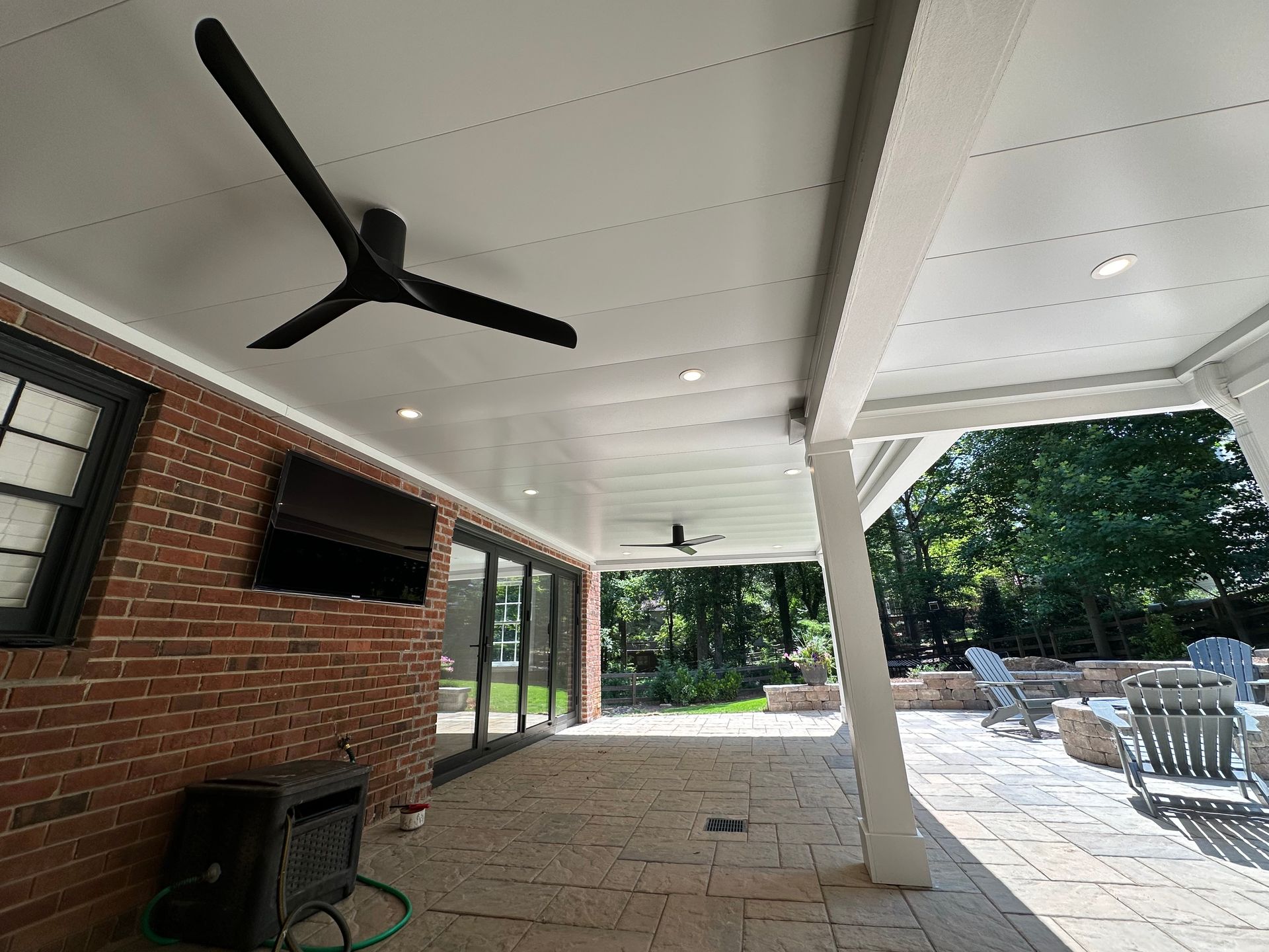 Covered patio with a black ceiling fan, brick wall with a TV, and outdoor seating.