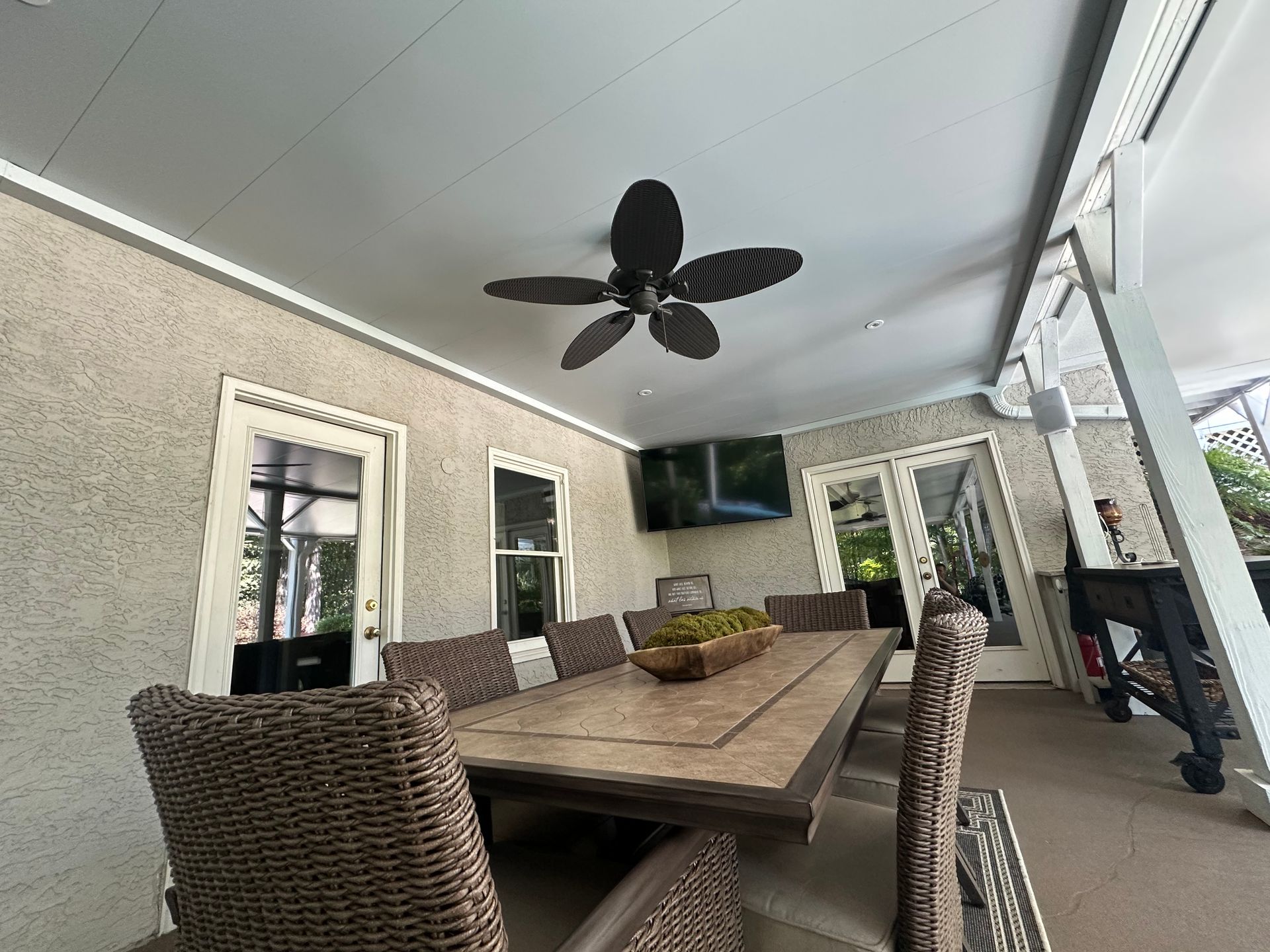 Covered patio with dining table, chairs, ceiling fan, and television.