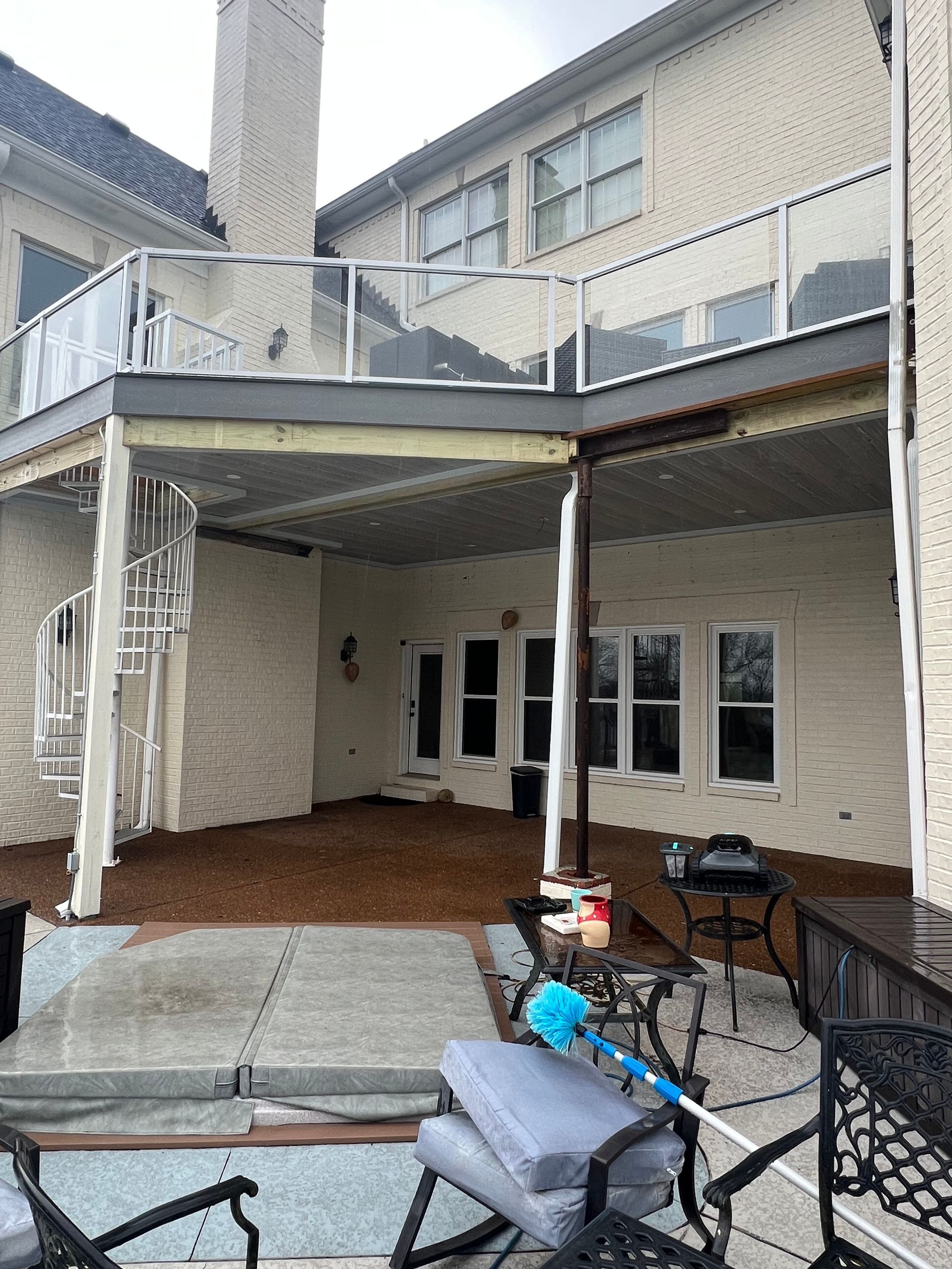 Multi-level deck attached to a brick house. Lower level patio with furniture, upper level with glass railing.