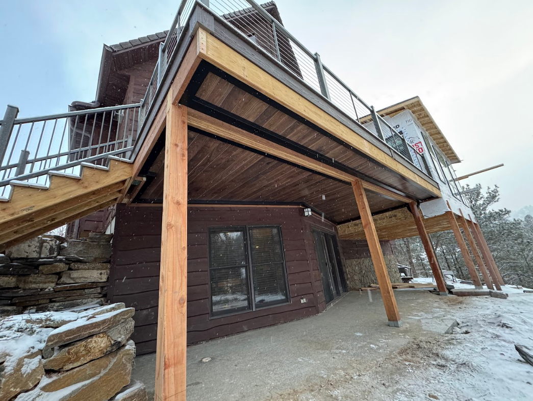 Wooden deck and stairs on a house with a snow-covered yard and a brown exterior.