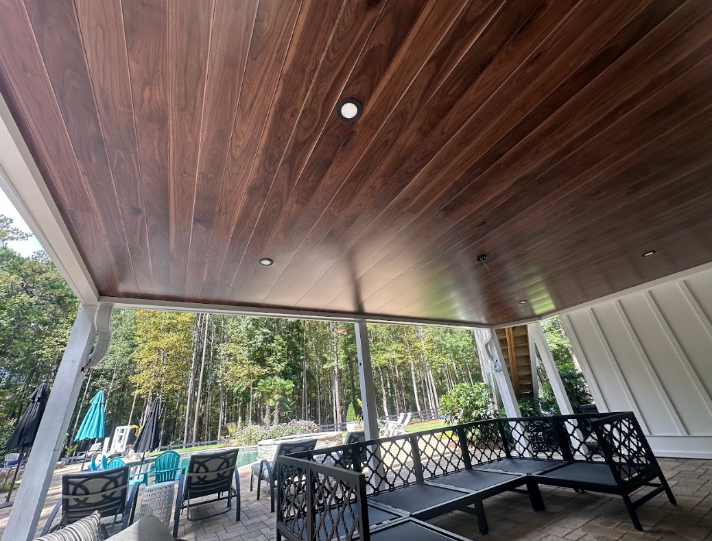 Wooden porch ceiling with recessed lights, overlooking a pool and trees.