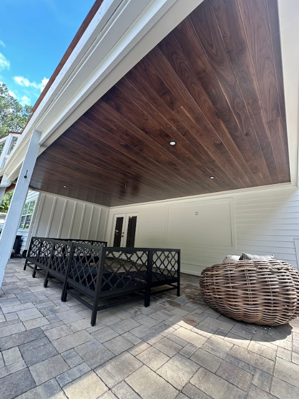 Outdoor patio with dark wood ceiling, white walls, black furniture, and woven basket on a stone floor.
