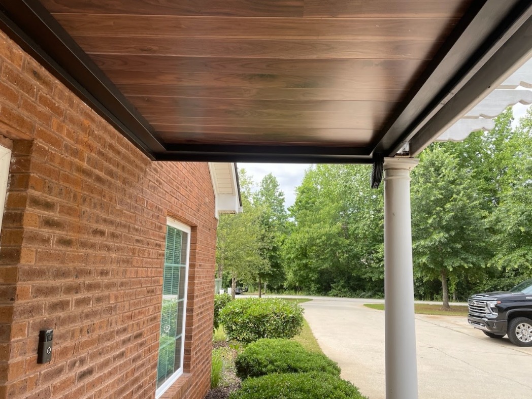 A brick building with a dark-framed, wood-paneled covered porch; a white column, trees, and a black pickup truck.
