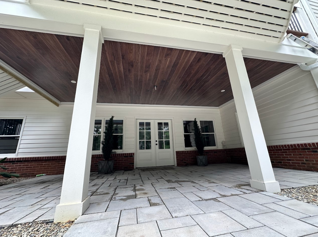 Covered outdoor patio with white columns, wood ceiling, stone floor, and double doors.