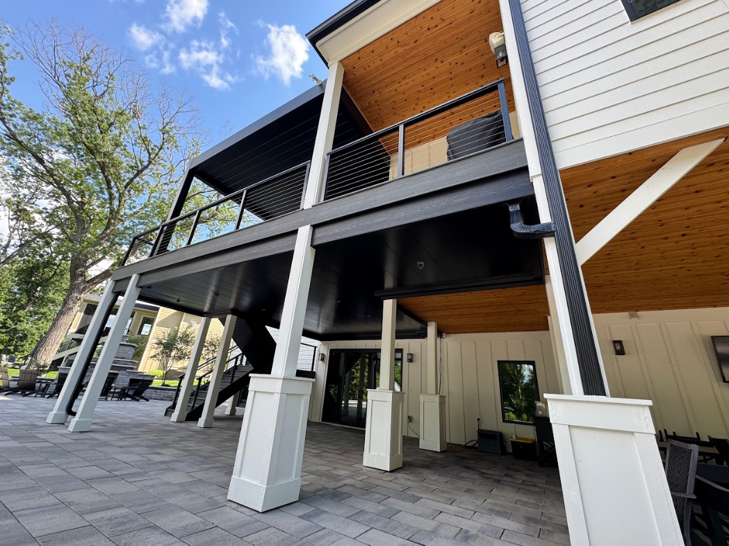 Exterior view of a modern white house with a black deck and columns on a sunny day.