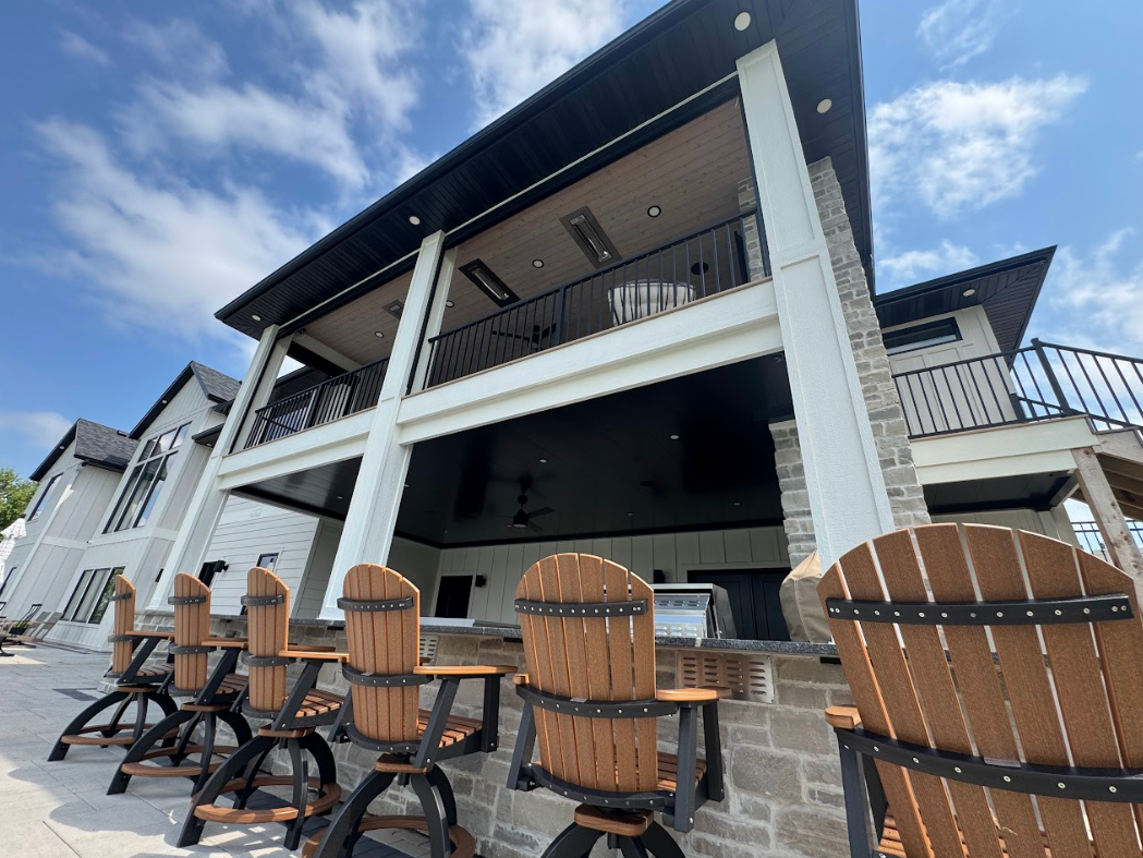 Outdoor bar area with wooden chairs under a two-story building with a black ceiling and white columns.