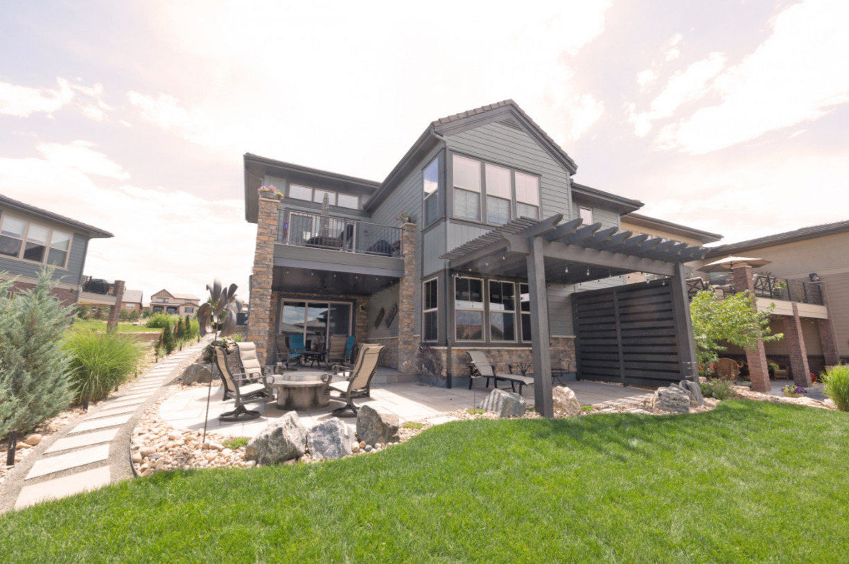 Two-story house with a patio, pergola, and fire pit in a backyard with green grass.