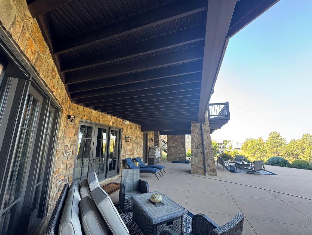 Covered outdoor patio with a concrete floor, stone columns, and wood beams.