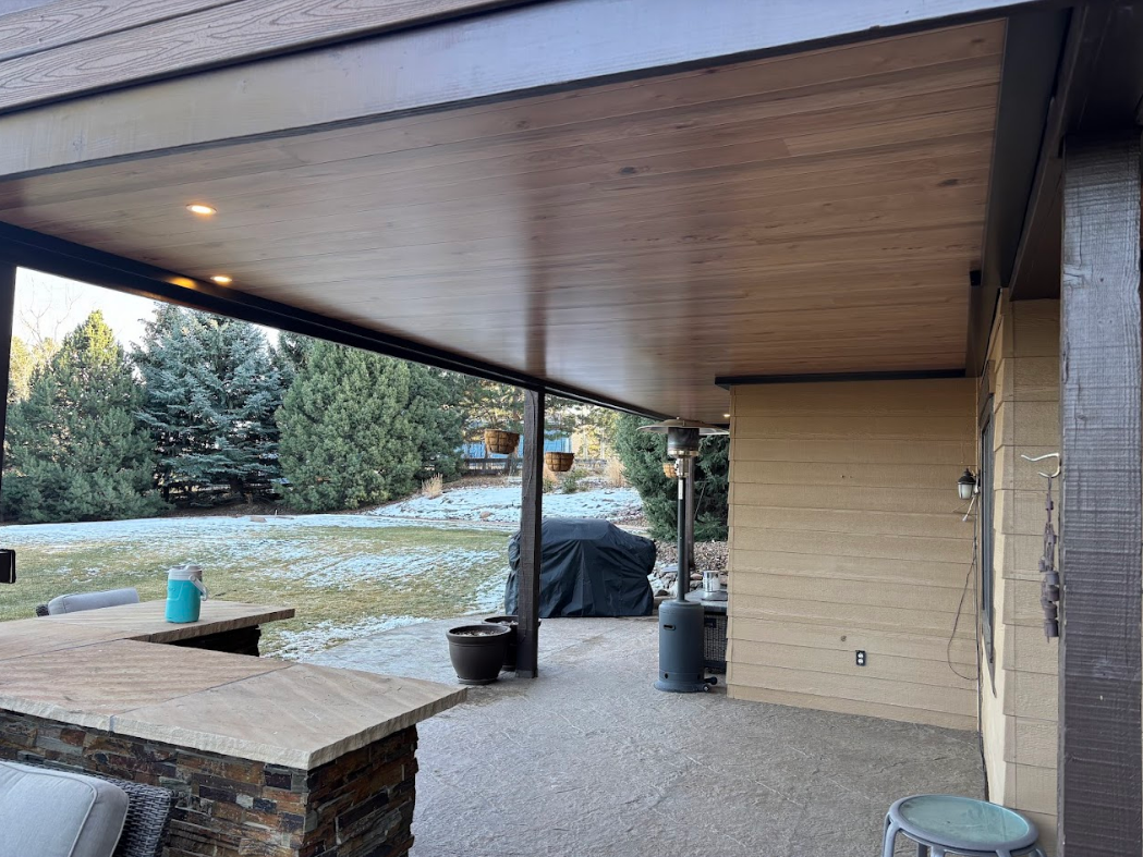 Outdoor patio with red sofa, stone fireplace, and dark ceiling.