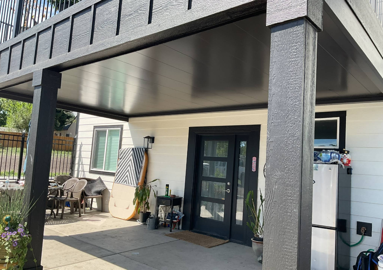 Covered patio with black supports and trim, white house, black door, and small patio furniture.