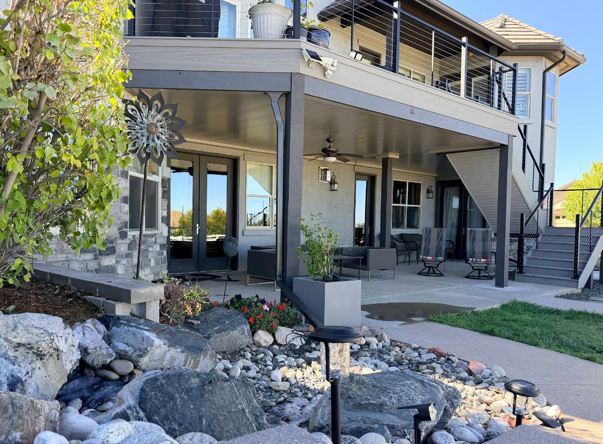 Backyard patio with a covered seating area under a second-story deck, beside a rock garden.