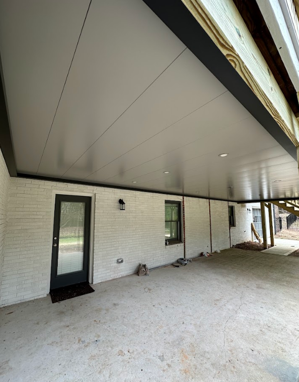 Covered patio with white brick wall, gray ceiling, black trim, and a black door.