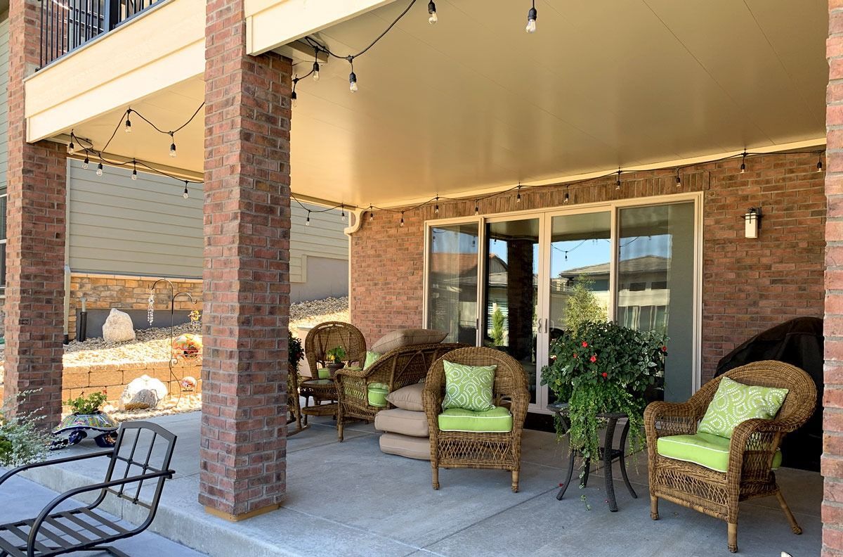 Patio with brick pillars, wicker furniture, and string lights. Sliding glass door and a small plant.