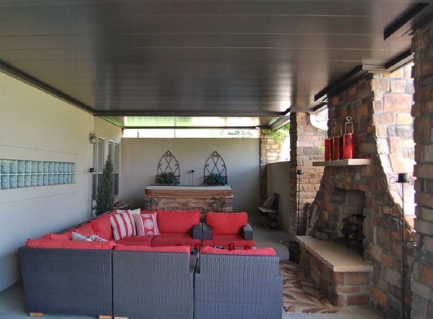 Outdoor patio with red sofa, stone fireplace, and dark ceiling.
