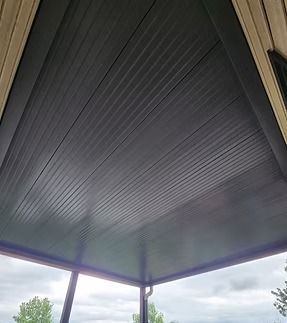 A dark gray patio roof with horizontal lines, viewed from below, over a light sky.