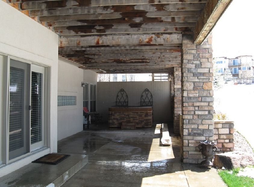 Covered outdoor patio with a concrete floor, stone columns, and wood beams.