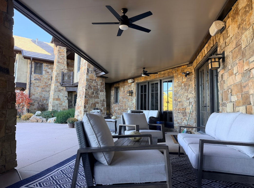 Patio with seating under a covered roof, stone walls, and ceiling fans.