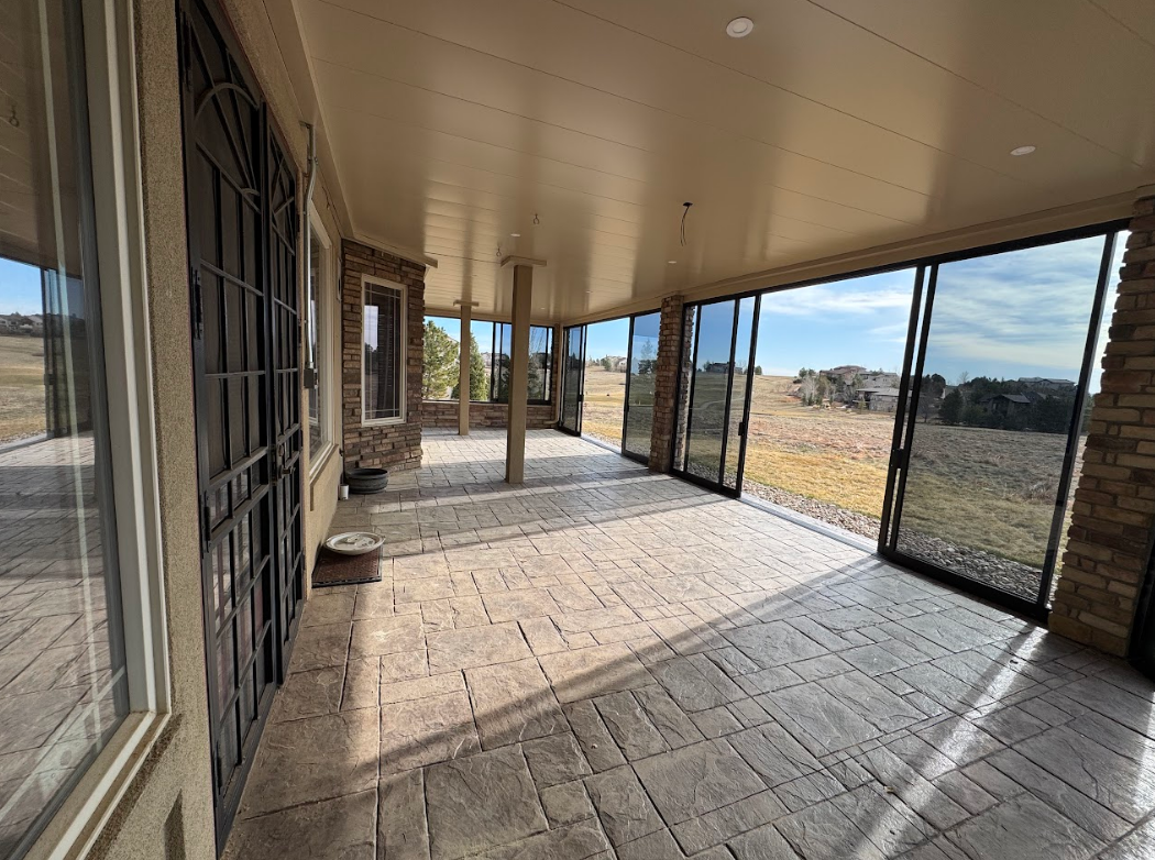 Covered patio with large sliding glass doors, stamped concrete floor, and scenic outdoor view.