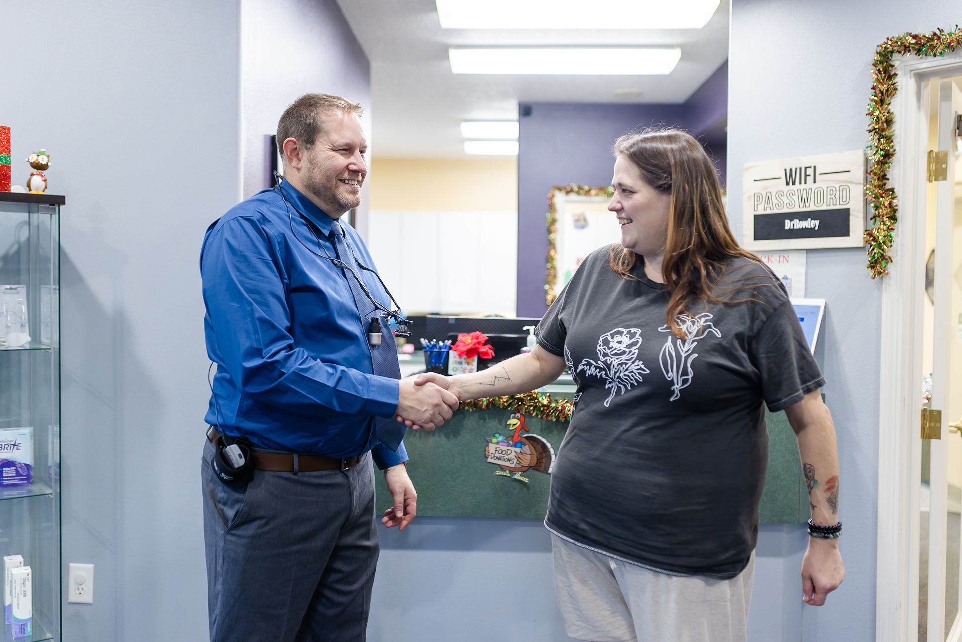 A man in blue shirt shakes hands with a woman in a gray tee; they're in a vet clinic with a counter.