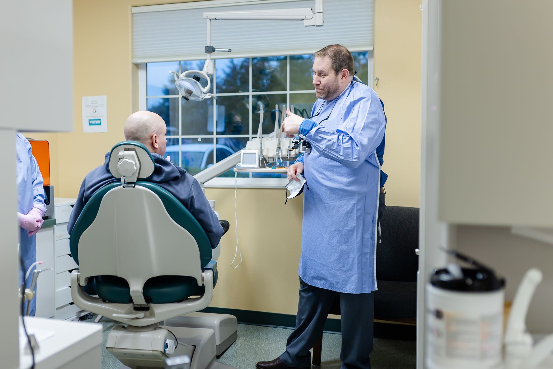 Dentist in blue gown consults a patient seated in a dental chair. Office setting.