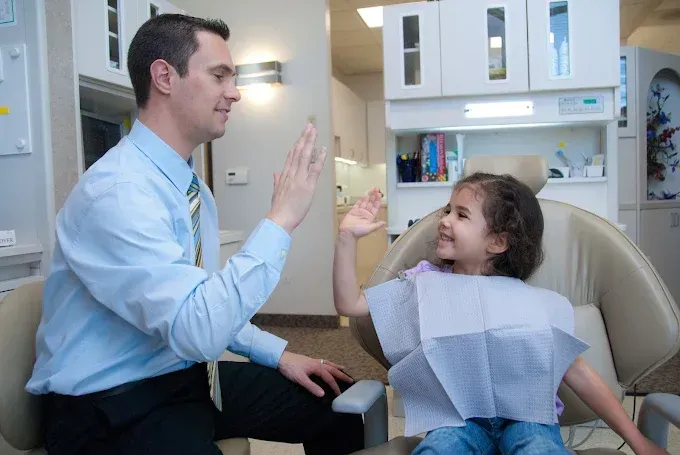 Dentist giving a high five to a child in a dental chair. Office setting.