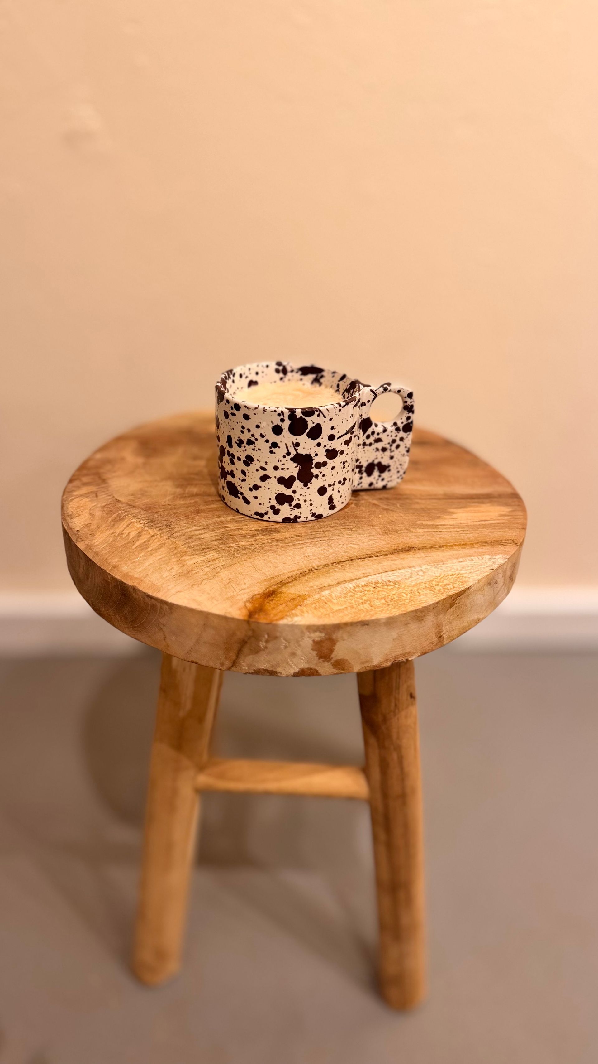 Een hartvormige kaars met zwart-witte spikkels staat op een klein houten krukje tegen een beige muur.