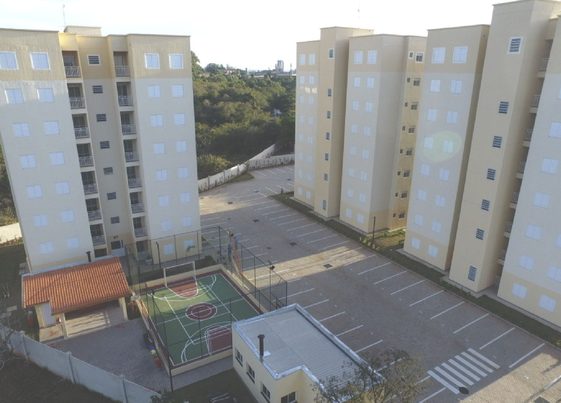 Complexo de apartamentos com prédios bege, uma quadra de basquete e um estacionamento.