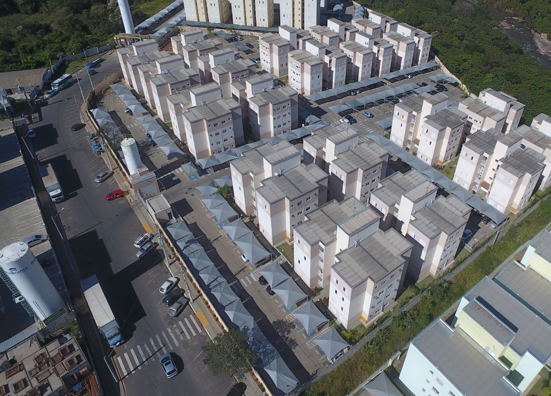 Vista aérea de um complexo de apartamentos com vários prédios bege, carros e árvores.