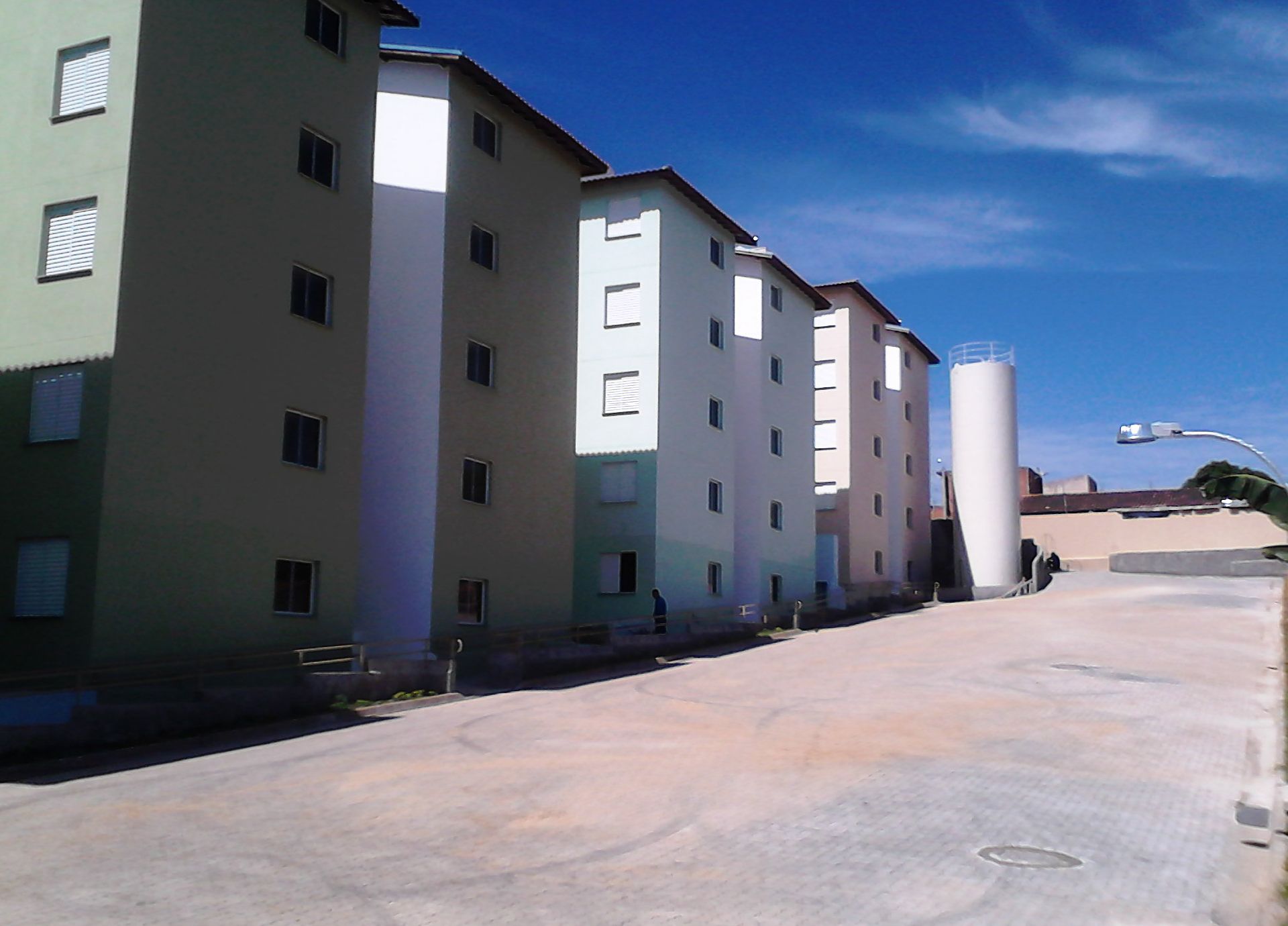 Prédios de apartamentos com cores variadas e detalhes em branco, erguidos em uma área pavimentada sob um céu azul.