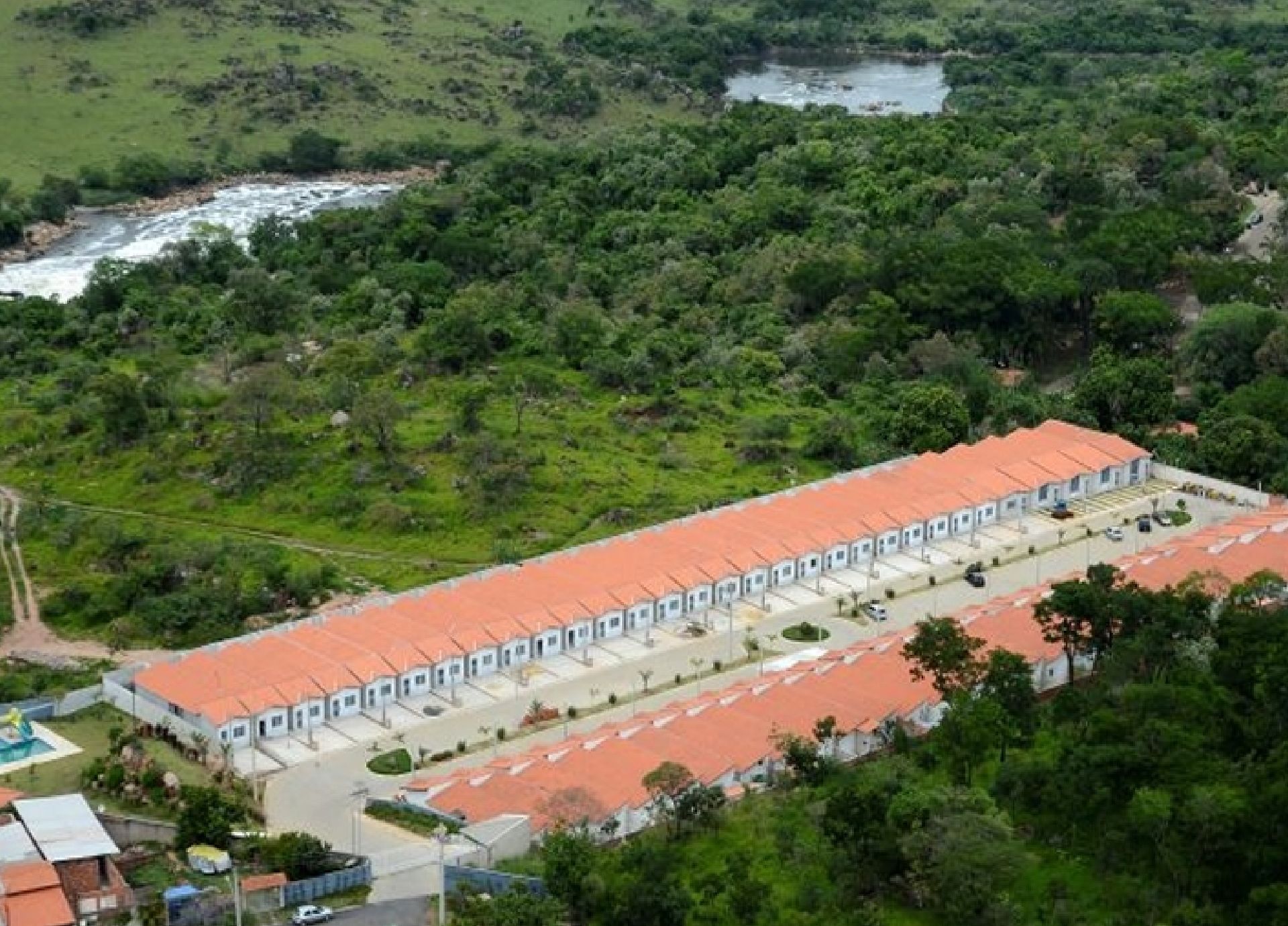 Casas geminadas com telhados laranja perto de um rio e árvores verdejantes.