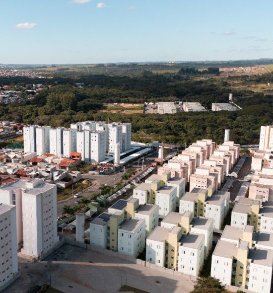 Vista aérea de um complexo residencial com edifícios em tons pastéis e um cenário de árvores sob um céu limpo.
