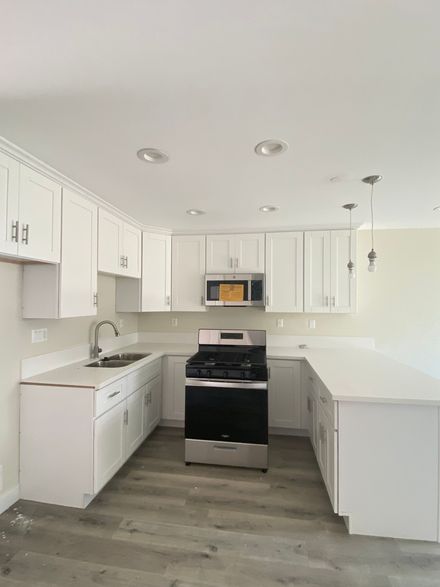 A kitchen with white cabinets , a stove , a sink , and a microwave.