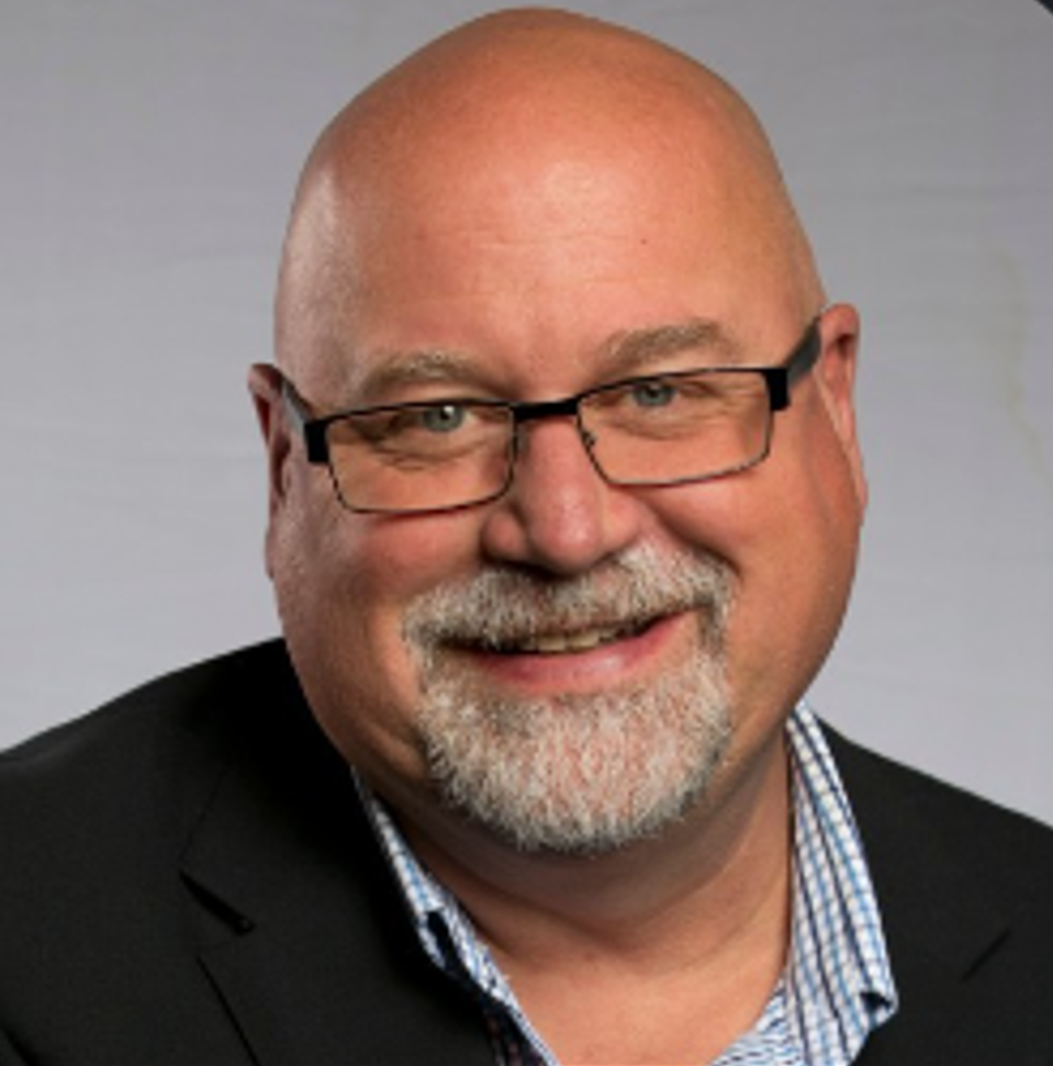 A bald man with glasses and a beard smiles for the camera