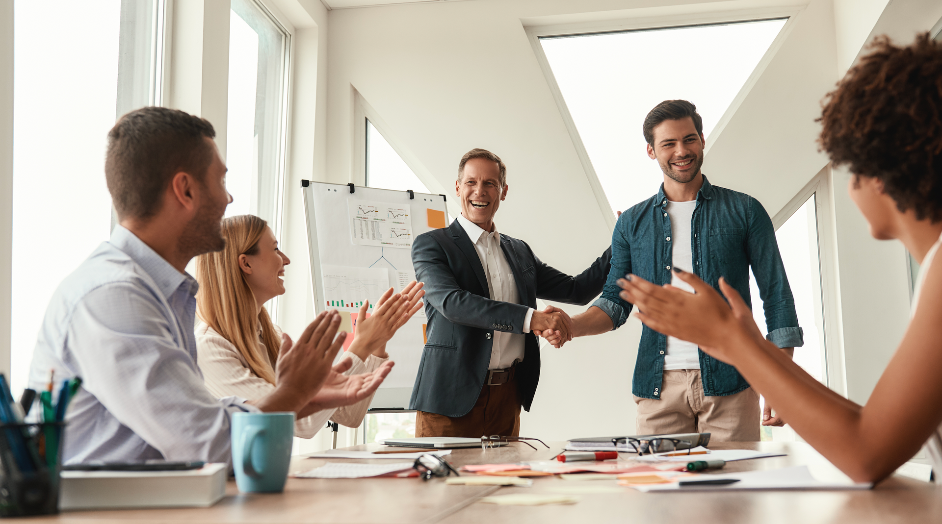 A group of people are sitting around a table shaking hands.