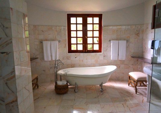 A clawfoot bathtub underneath a window in a bathroom with newly installed marble tile floors and tile walls