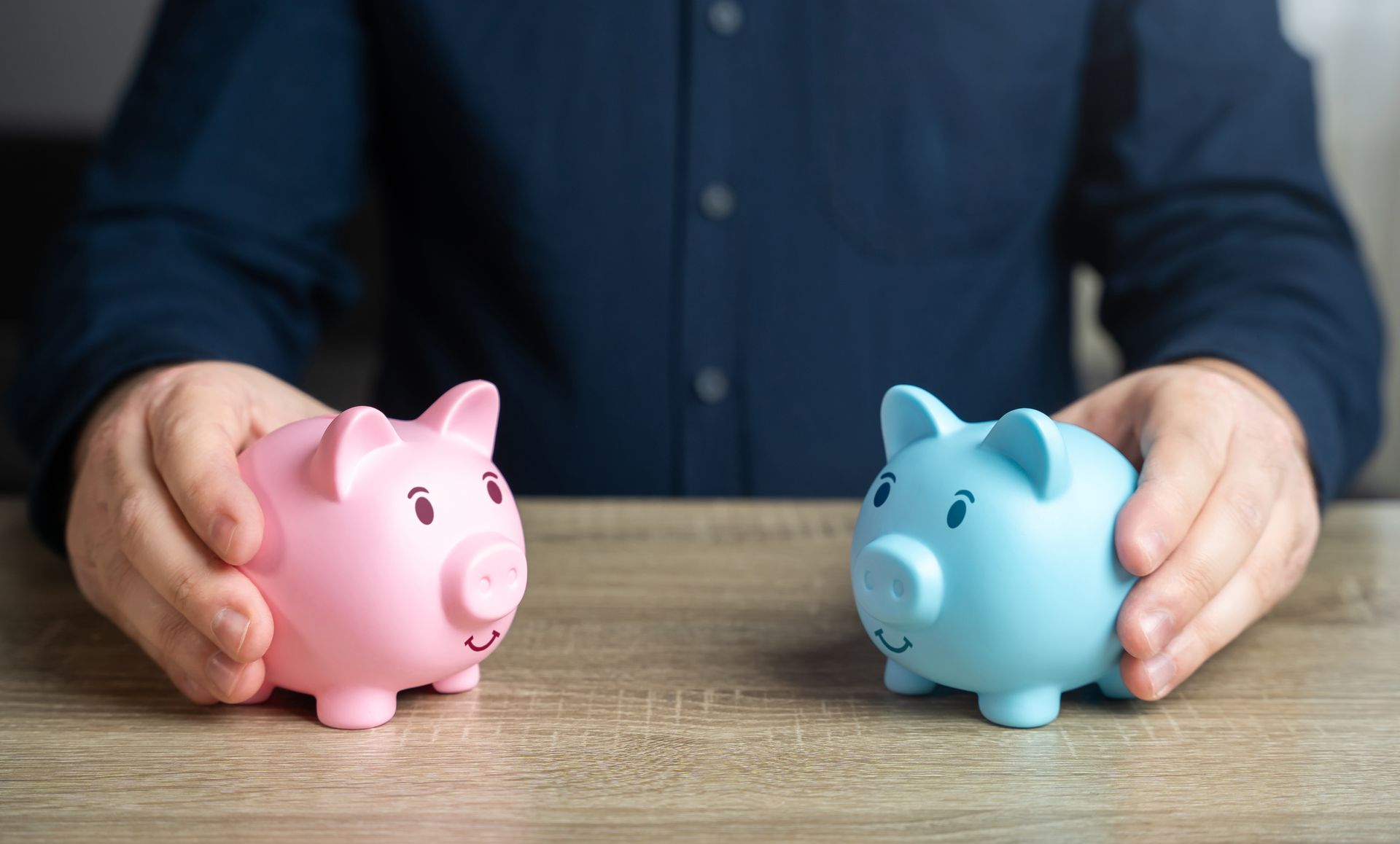 Hands holding pink and blue piggy banks on a wooden table