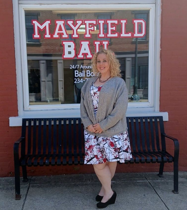 A woman is standing in front of a mayfield bail sign