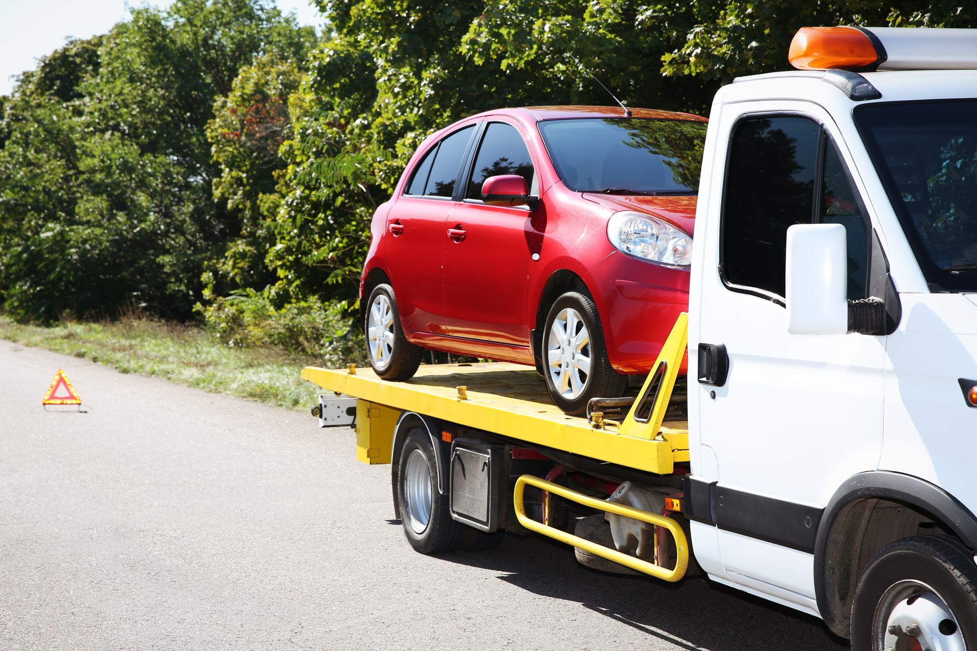 A red car is being towed by a tow truck.