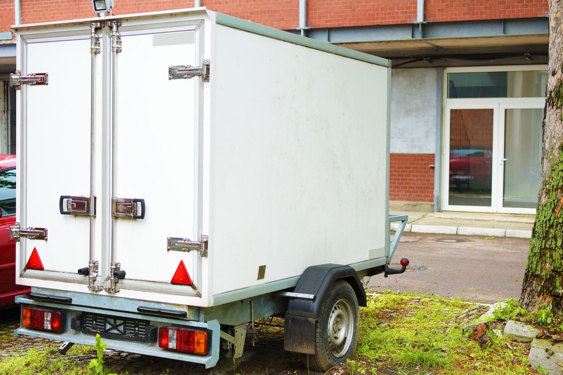 A white trailer is parked in front of a brick building.