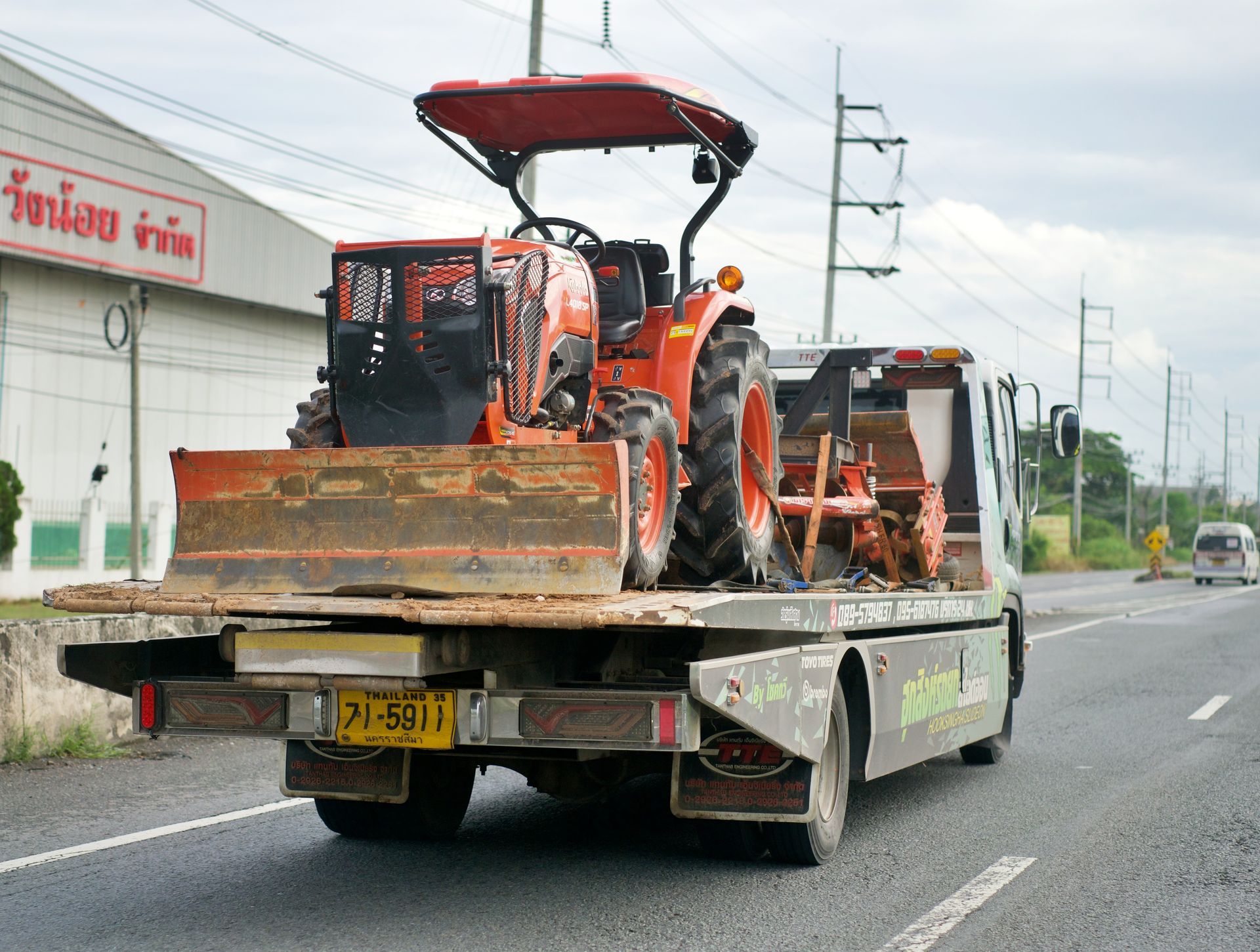 A tow truck is carrying a tractor on the back of it.