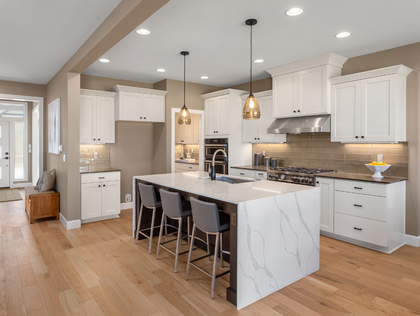 Bright white kitchen with a marble-topped island, wooden floors, and pendant lighting.