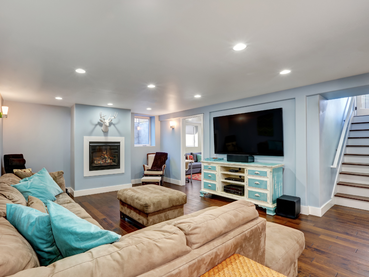 Living room with blue walls, fireplace, TV, and sectional sofa. Brown floors, stairs to the right.