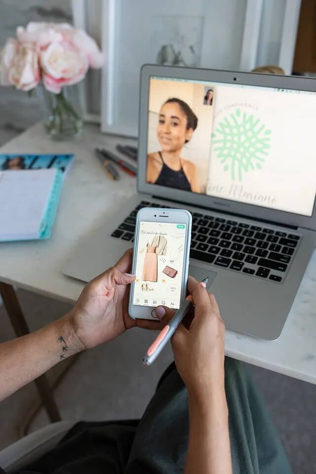 A woman is holding a cell phone in front of a laptop computer.