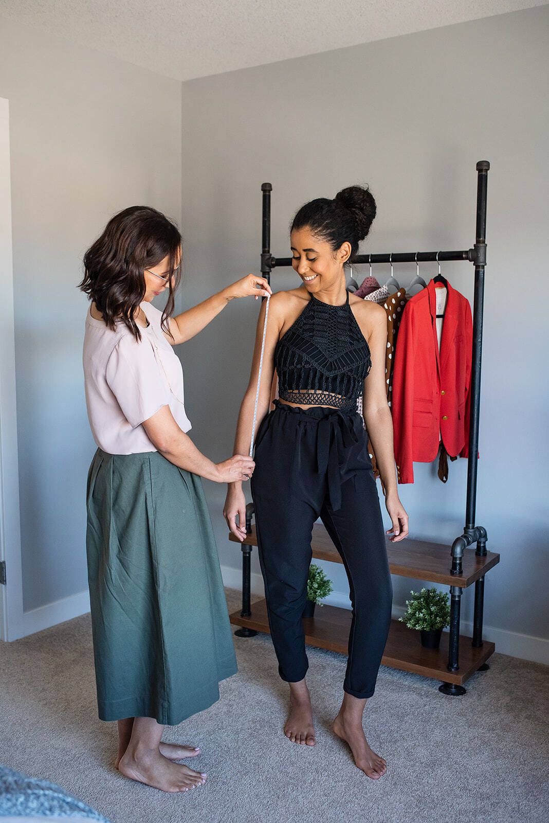 A woman is measuring another woman 's arm in a room.