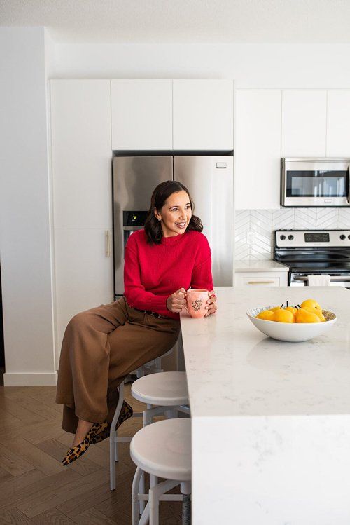 A woman is sitting on a stool in a kitchen holding a cup of coffee.