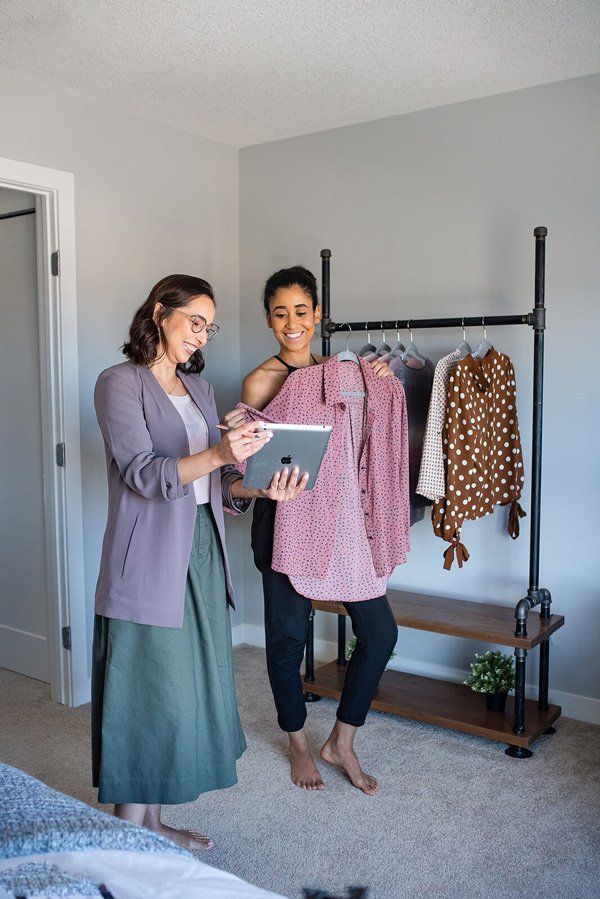 Two women are standing next to each other in a bedroom looking at a tablet.