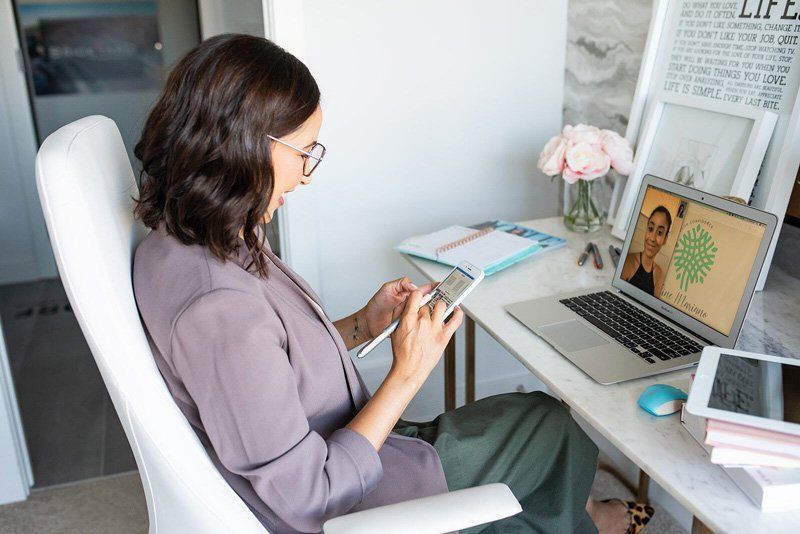 A woman is sitting at a desk with a laptop and a tablet.